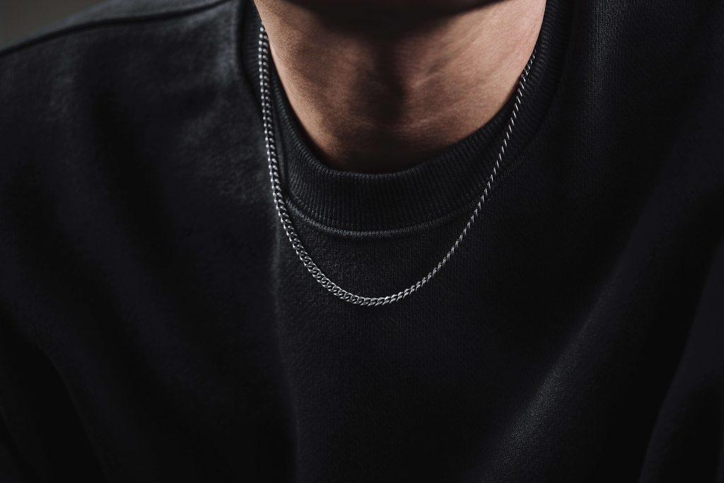 close up image of a silver mens necklace against a black jumper.